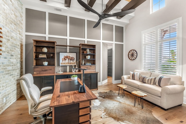 office with light hardwood / wood-style floors, brick wall, ceiling fan, and a high ceiling