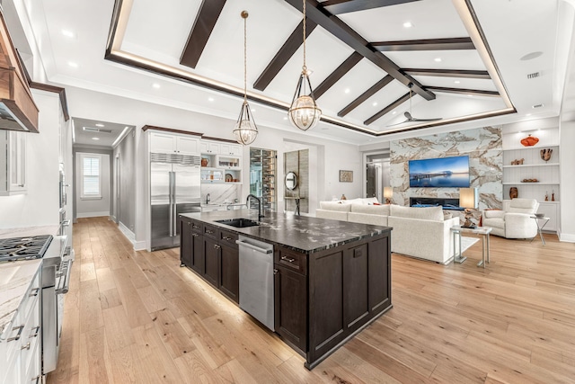 kitchen with sink, dark stone countertops, white cabinets, high end appliances, and a center island with sink