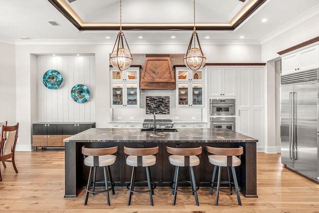 kitchen featuring stainless steel appliances, light hardwood / wood-style flooring, pendant lighting, and custom exhaust hood