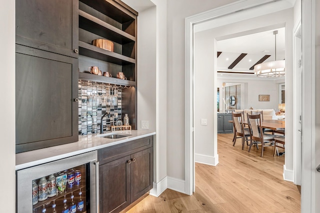 bar with beverage cooler, pendant lighting, light wood-type flooring, sink, and dark brown cabinetry