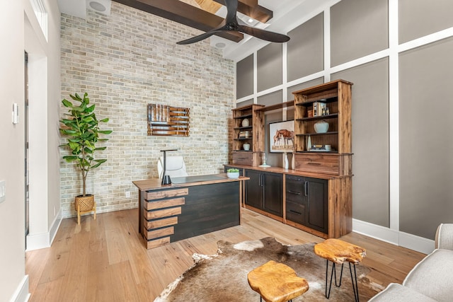 office area with a high ceiling, ceiling fan, brick wall, and light hardwood / wood-style floors