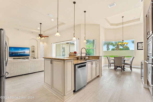 kitchen featuring light stone counters, a kitchen island with sink, sink, appliances with stainless steel finishes, and decorative light fixtures