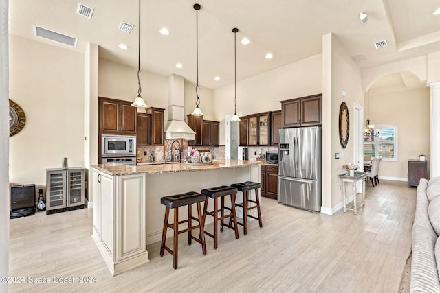 kitchen featuring light stone counters, pendant lighting, custom exhaust hood, an island with sink, and appliances with stainless steel finishes