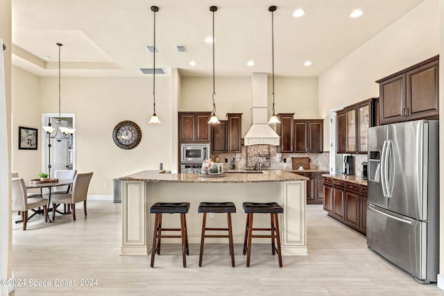 kitchen featuring pendant lighting, stainless steel appliances, light stone countertops, and a kitchen island with sink