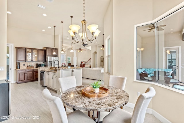 dining area with ceiling fan with notable chandelier, a towering ceiling, light hardwood / wood-style flooring, and sink