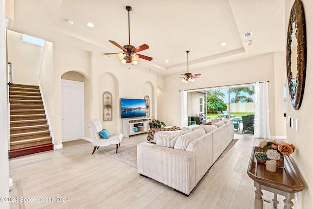 living room with ceiling fan, a tray ceiling, and light hardwood / wood-style flooring