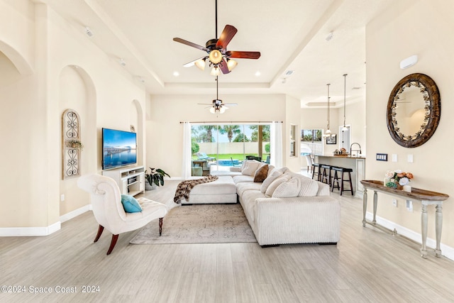 living room with ceiling fan, a tray ceiling, and light hardwood / wood-style floors