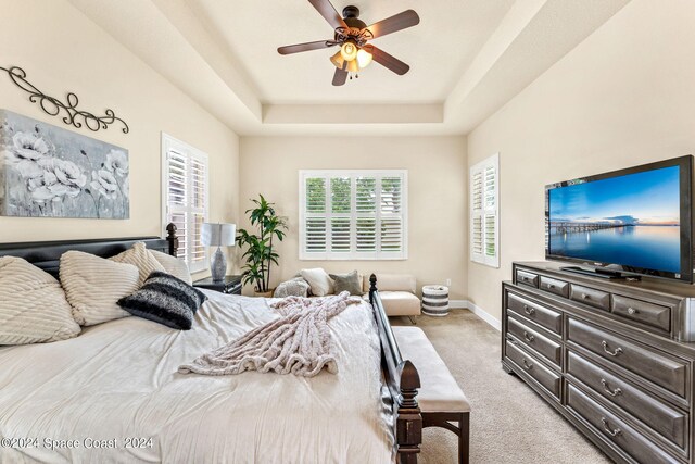 bedroom featuring light carpet, ceiling fan, and a raised ceiling