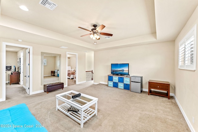 carpeted living room with ceiling fan and a tray ceiling