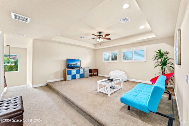 living area featuring ceiling fan, carpet floors, and a tray ceiling