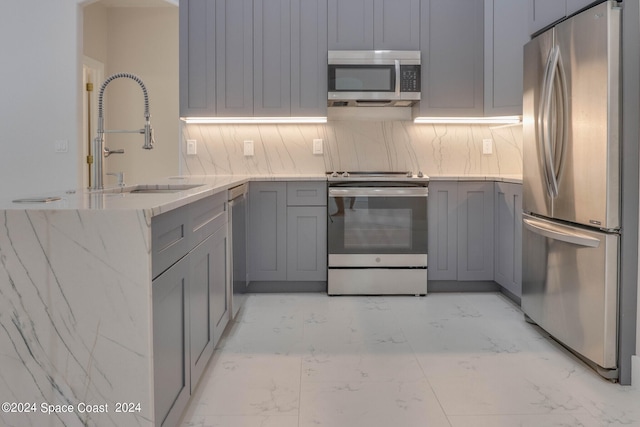 kitchen featuring sink, kitchen peninsula, gray cabinetry, backsplash, and stainless steel appliances