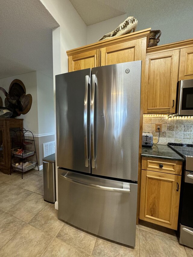 kitchen featuring light tile patterned flooring, appliances with stainless steel finishes, tasteful backsplash, and dark stone counters