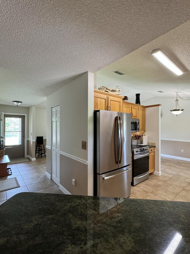 kitchen with a textured ceiling, light tile patterned floors, and stainless steel appliances