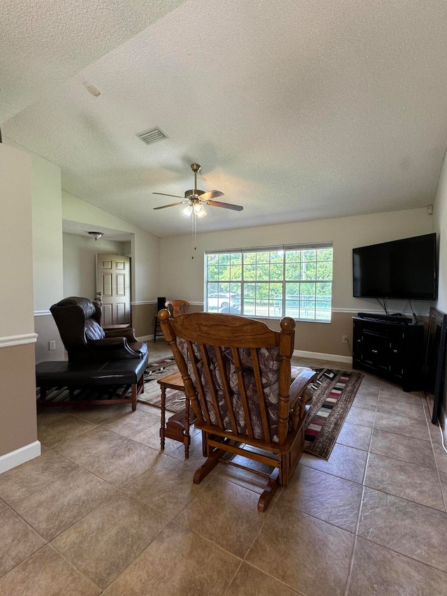 living room with a textured ceiling, ceiling fan, light tile patterned floors, and lofted ceiling