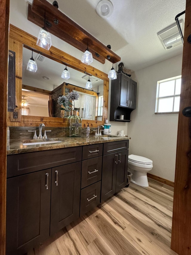 bathroom featuring a textured ceiling, hardwood / wood-style floors, dual vanity, and toilet