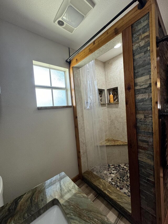 bathroom with hardwood / wood-style flooring, a textured ceiling, tiled shower, and toilet