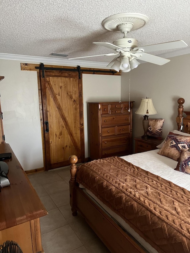 tiled bedroom featuring ceiling fan, a barn door, ornamental molding, and a textured ceiling