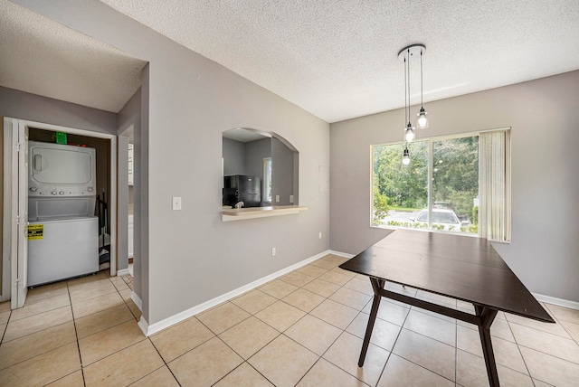 unfurnished dining area featuring a textured ceiling, stacked washing maching and dryer, and light tile patterned floors