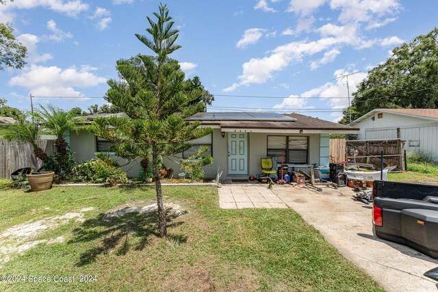 rear view of property with solar panels, a lawn, fence, and stucco siding