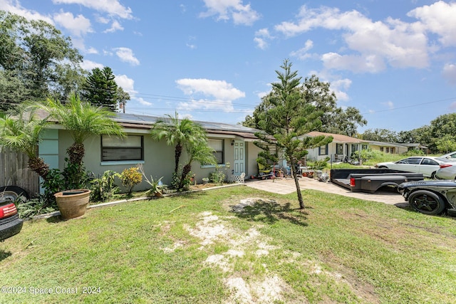 ranch-style house with a front yard, roof mounted solar panels, and stucco siding