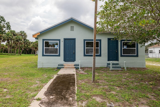 bungalow-style home with entry steps, a front lawn, and stucco siding