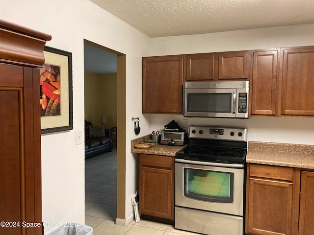 kitchen featuring appliances with stainless steel finishes, light tile patterned flooring, and a textured ceiling