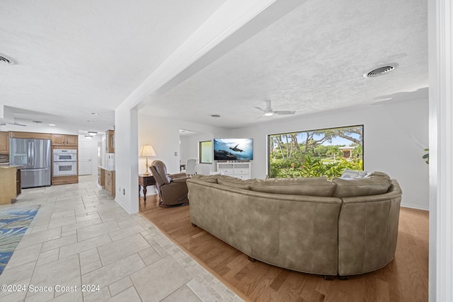 living room with light hardwood / wood-style floors, ceiling fan, and a textured ceiling