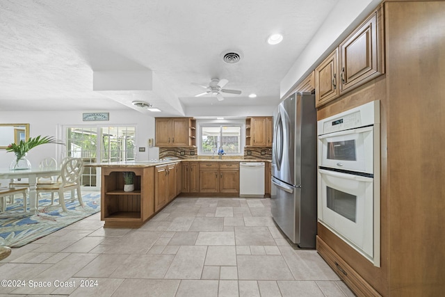 kitchen with backsplash, light tile patterned floors, white appliances, ceiling fan, and kitchen peninsula