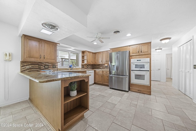 kitchen featuring ceiling fan, dark stone counters, tasteful backsplash, kitchen peninsula, and white appliances