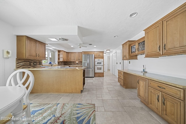 kitchen featuring backsplash, light tile patterned flooring, light stone countertops, stainless steel fridge, and double oven