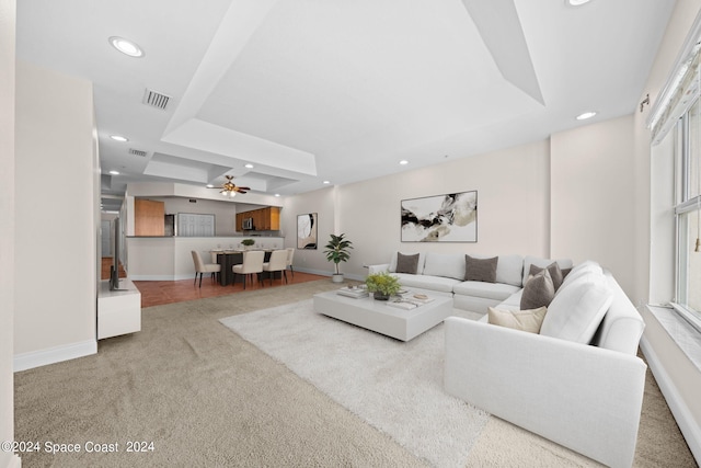 carpeted living room featuring ceiling fan and a raised ceiling