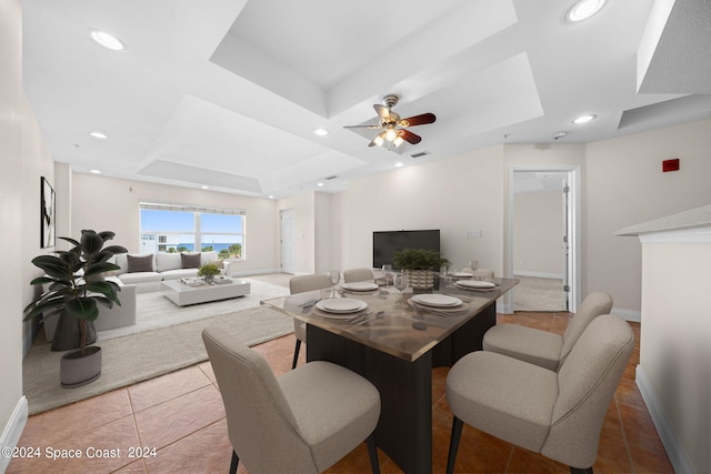 dining space with a raised ceiling, light tile patterned floors, and ceiling fan