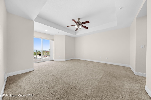 unfurnished room featuring a tray ceiling, light colored carpet, and ceiling fan