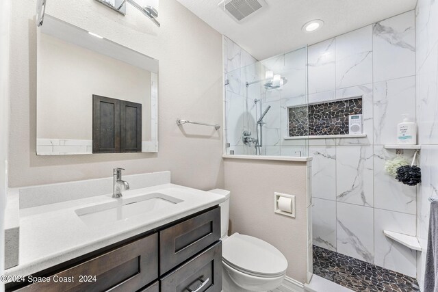 bathroom with a tile shower, vanity, and toilet