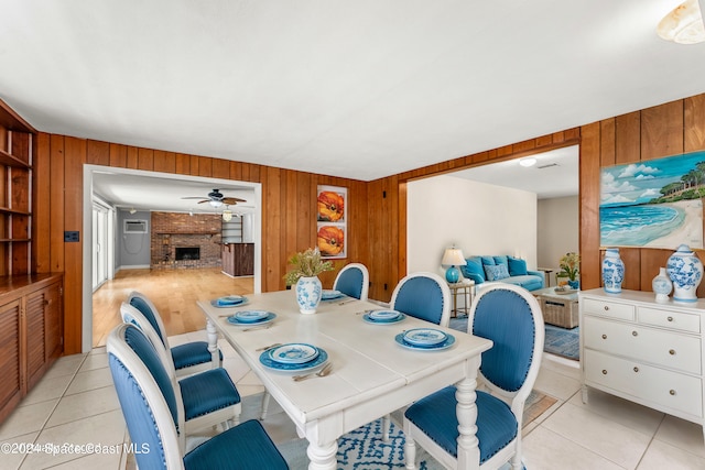 tiled dining area featuring ceiling fan, wooden walls, and a fireplace