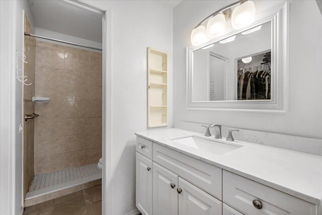 bathroom with toilet, tiled shower, vanity, and tile patterned floors