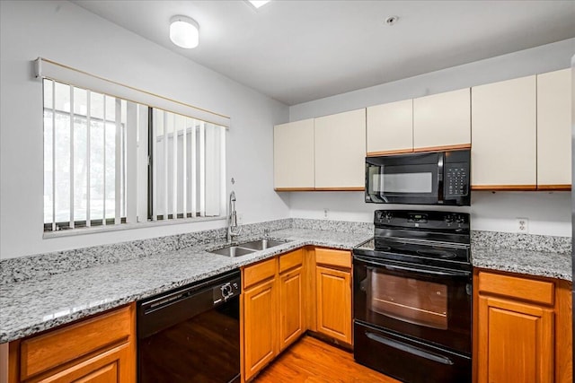 kitchen with sink, light stone counters, black appliances, and light hardwood / wood-style flooring