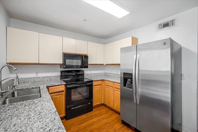 kitchen with sink, hardwood / wood-style floors, black appliances, and light stone countertops