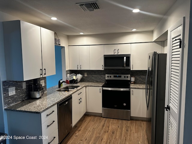 kitchen with appliances with stainless steel finishes, white cabinets, sink, and light wood-type flooring