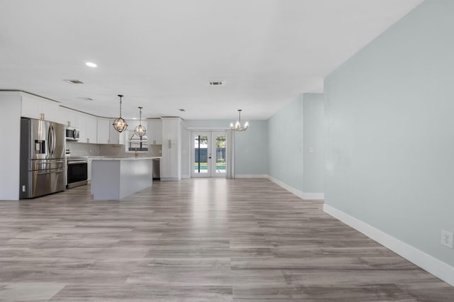 unfurnished living room with a notable chandelier, light wood-type flooring, and french doors