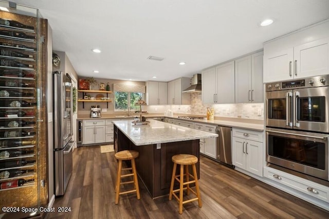 kitchen featuring appliances with stainless steel finishes, white cabinetry, a kitchen island, and wall chimney range hood