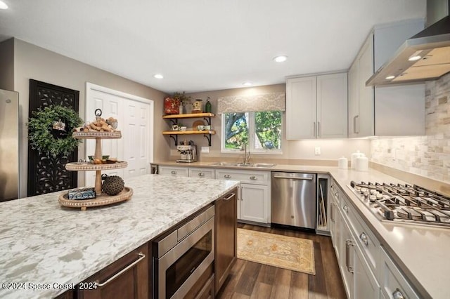 kitchen featuring sink, dark wood-type flooring, stainless steel appliances, wall chimney range hood, and light stone counters