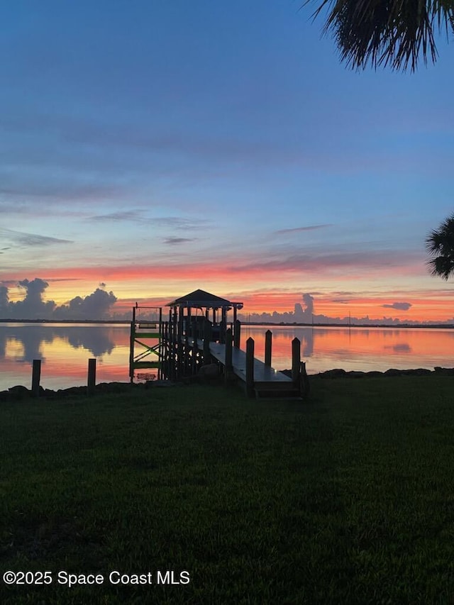 view of dock with a lawn and a water view