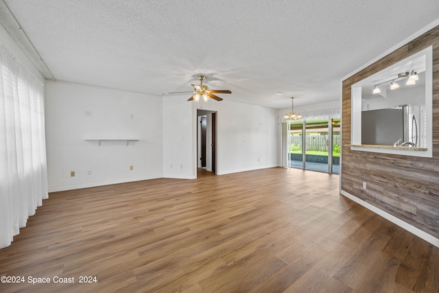 unfurnished living room featuring wood-type flooring, ceiling fan with notable chandelier, and a textured ceiling