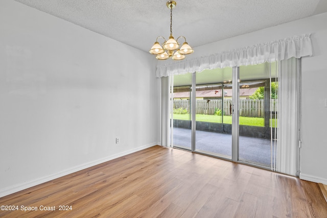 empty room featuring a textured ceiling, an inviting chandelier, and hardwood / wood-style floors