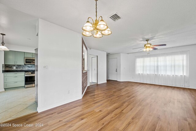 unfurnished living room with a textured ceiling, ceiling fan with notable chandelier, and light hardwood / wood-style floors