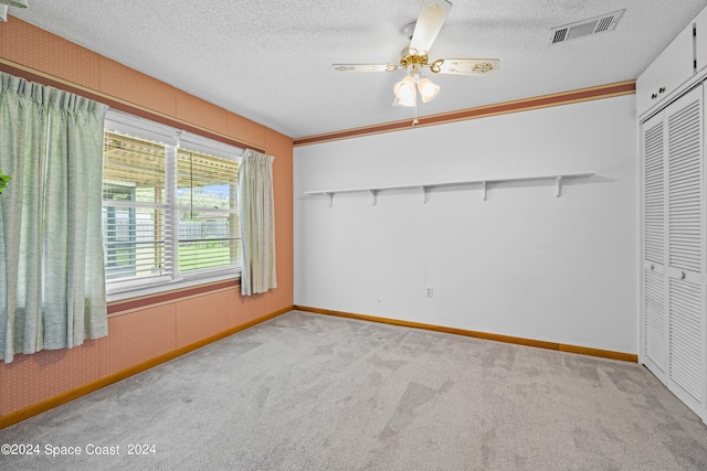 unfurnished bedroom featuring ceiling fan, a textured ceiling, light carpet, and a closet