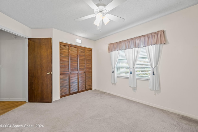 unfurnished bedroom with a textured ceiling, a closet, ceiling fan, and carpet floors