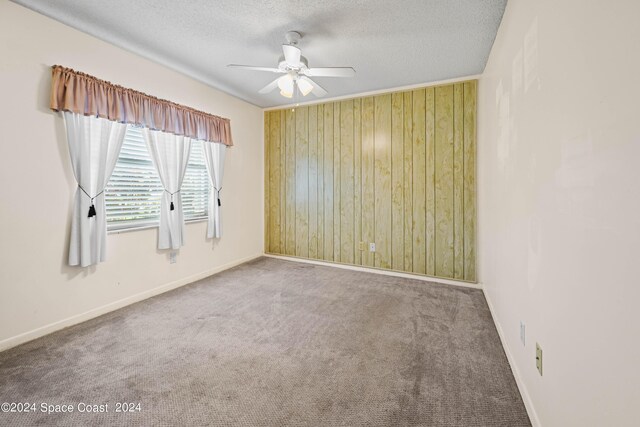 unfurnished room featuring ceiling fan, wood walls, a textured ceiling, and carpet floors