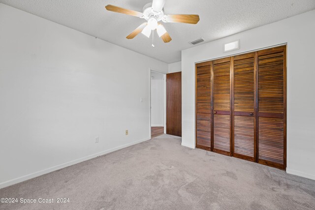 unfurnished bedroom featuring ceiling fan, a textured ceiling, light colored carpet, and a closet